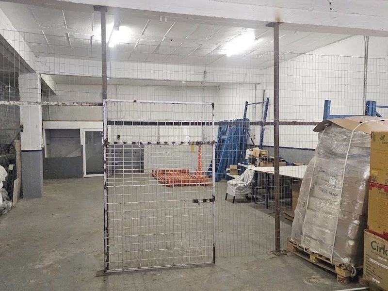 Industrial warehouse space featuring concrete flooring, exposed ceiling beams, and secure wire mesh partitioning for storage or operational use.
