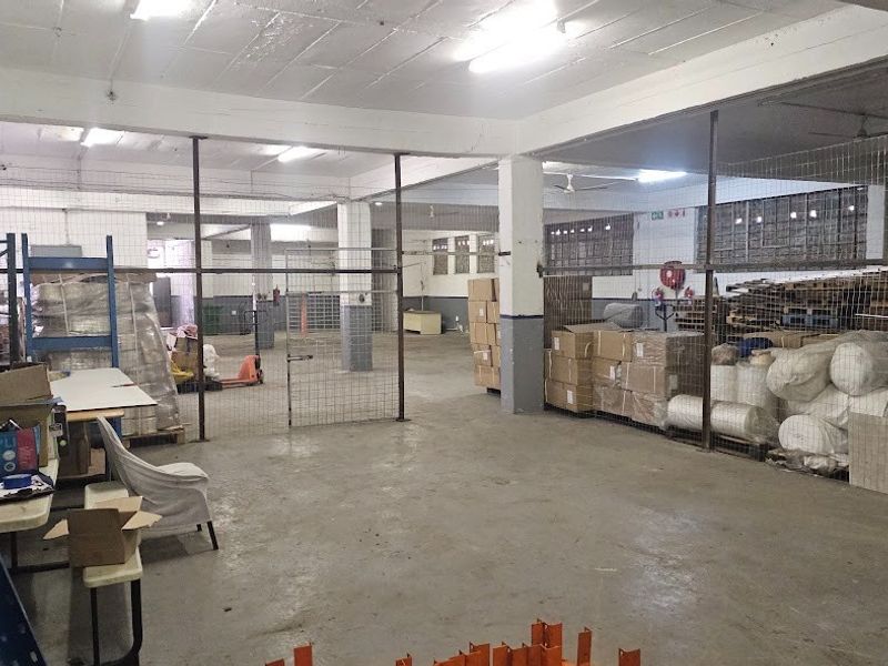 Spacious industrial warehouse area featuring concrete flooring, exposed structural columns, and wire mesh partitioning for secure storage zones.