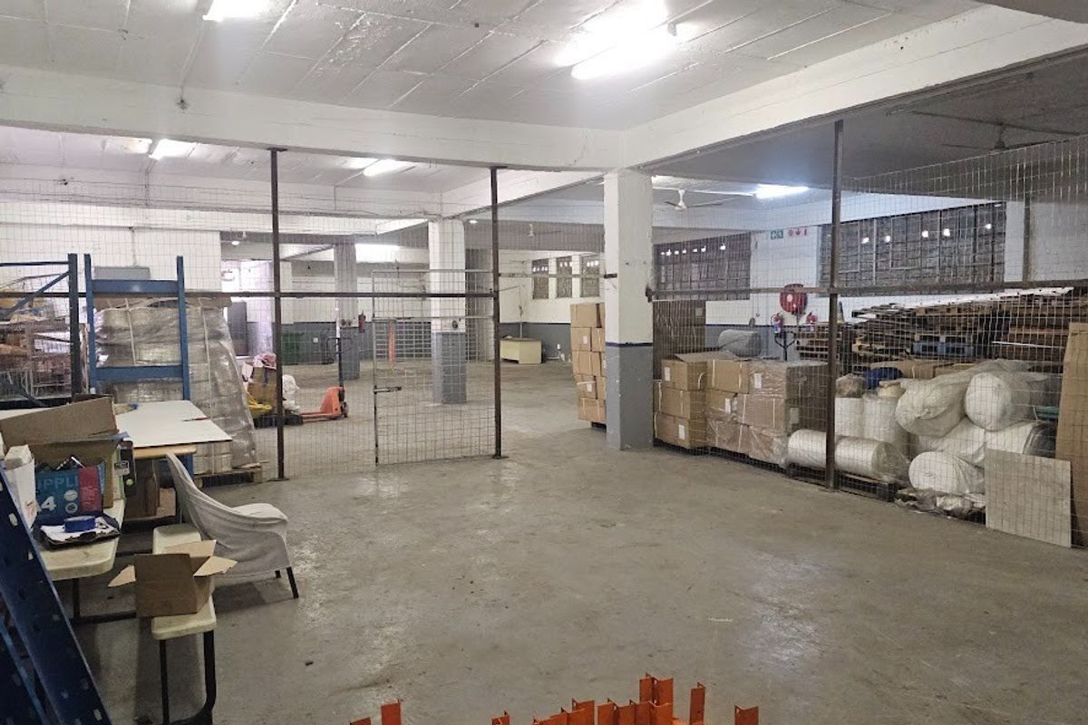 Spacious industrial warehouse area featuring concrete flooring, exposed structural columns, and wire mesh partitioning for secure storage zones.