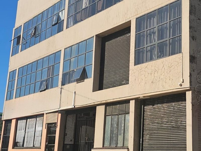 Multi-story industrial building facade featuring large grid-style windows, roller shutter doors, and secure metal entrance gates.
