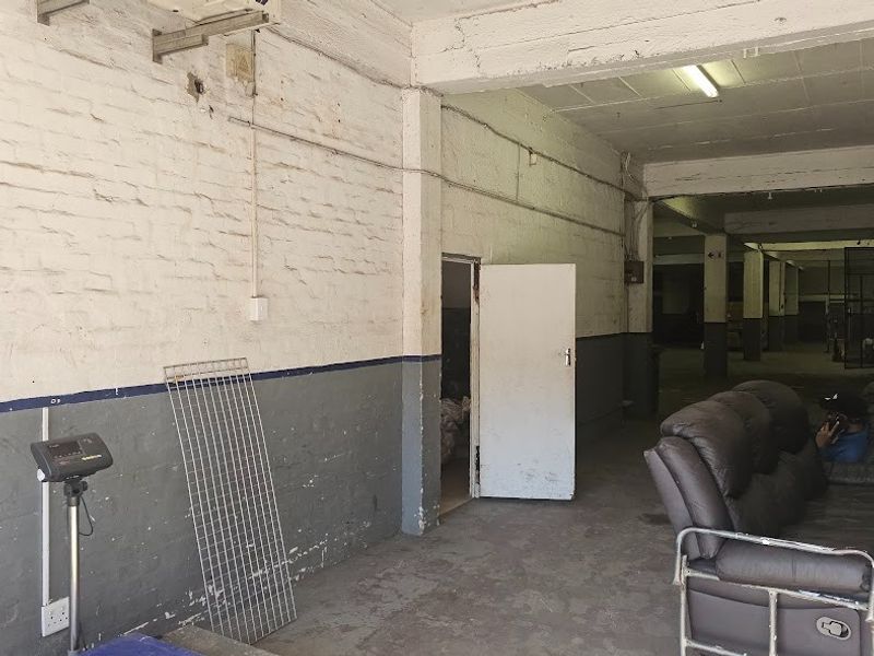 Industrial warehouse space featuring exposed brick walls, concrete flooring, and high-ceiling structure, suitable for storage or workshop operations.