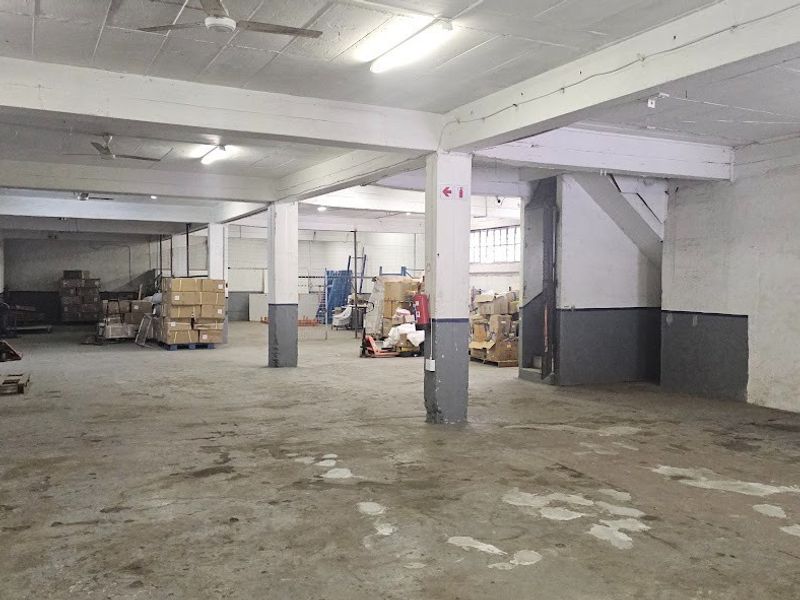 Spacious industrial warehouse area featuring high ceilings, concrete flooring, and structural support columns, suitable for storage or manufacturing operations.