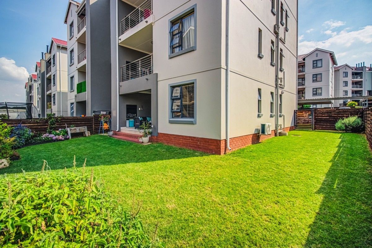 A view of the apartment building exterior featuring a private ground-floor garden, patio area, and well-maintained brick and plaster facade.