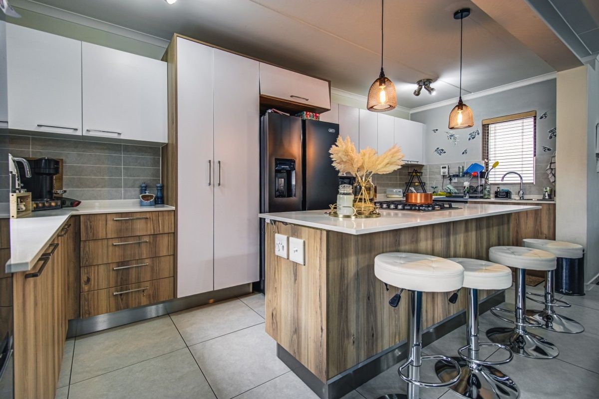 Modern kitchen featuring a central island with breakfast bar, stone countertops, two-tone cabinetry, and integrated gas hob, finished with tiled flooring.