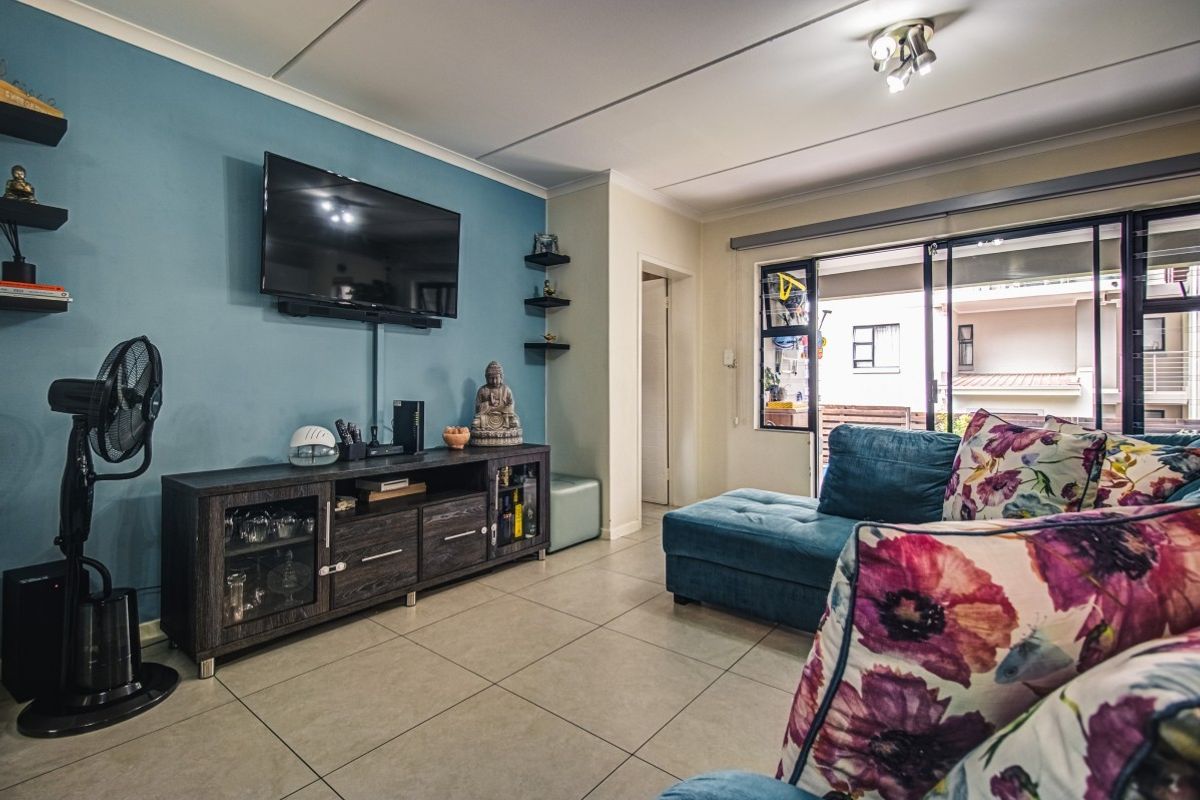 A well-maintained living room featuring large format floor tiles, a feature wall, and sliding glass doors providing access to an outdoor balcony area.
