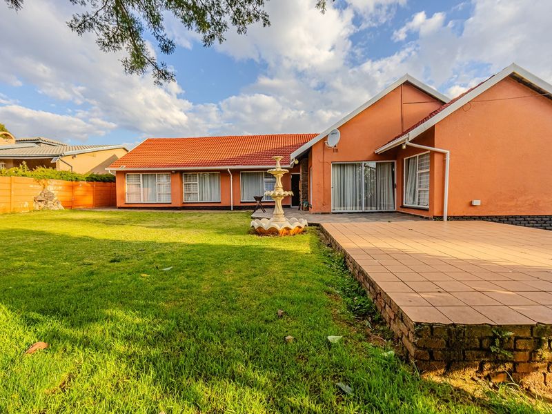 Rear view of the house featuring a tiled patio, landscaped lawn, and a central garden fountain.