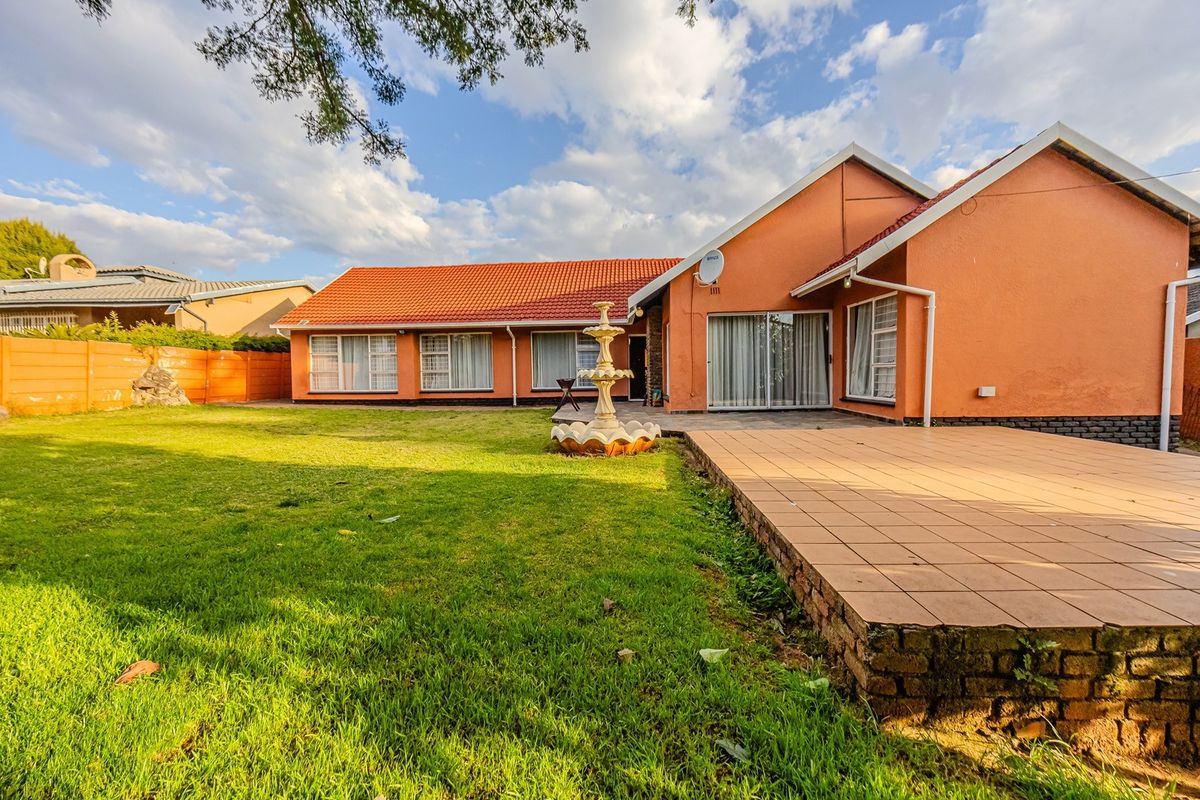 Rear view of the house featuring a tiled patio, landscaped lawn, and a central garden fountain.