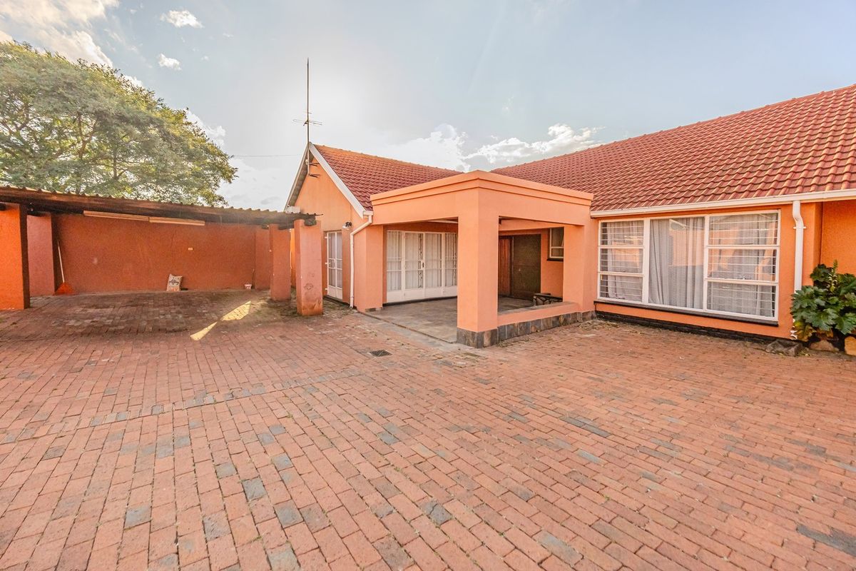 A rear exterior view of the house featuring a covered patio, brick-paved courtyard, and a timber pergola structure.
