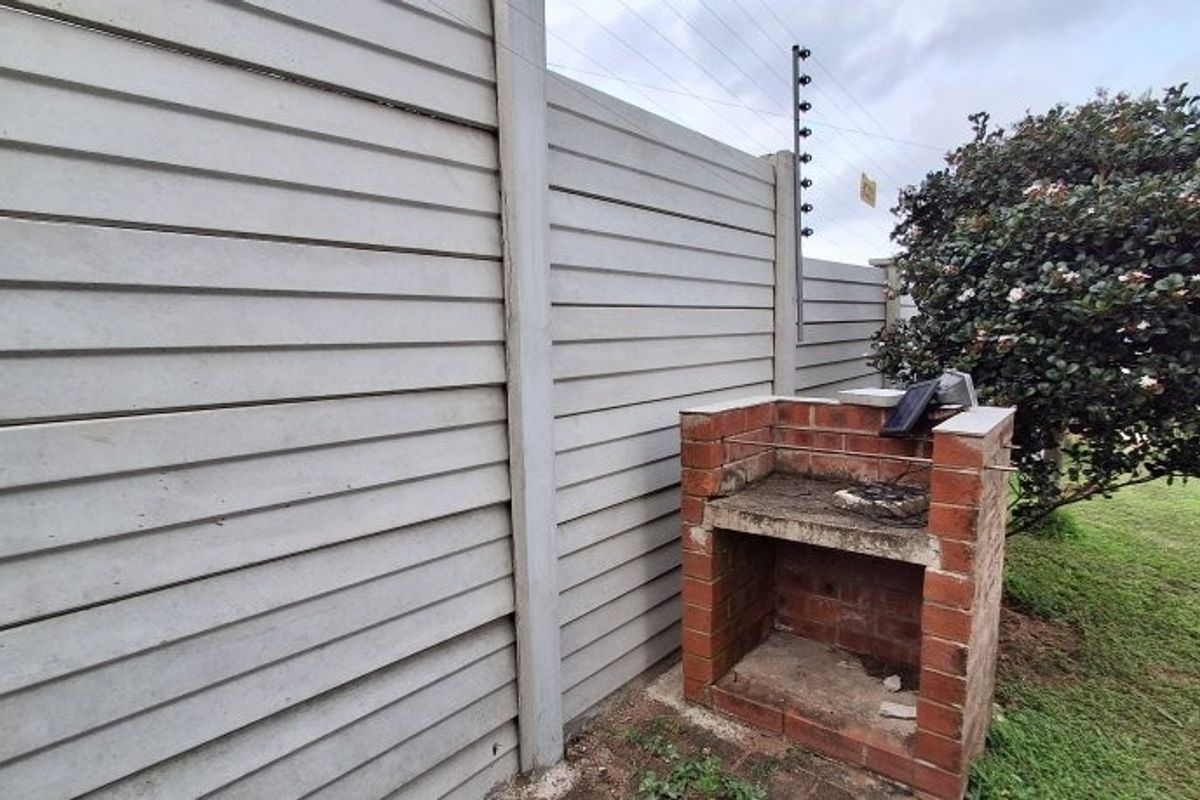 Outdoor area featuring a built-in brick braai or barbecue unit set against a precast concrete boundary wall with electric fencing.