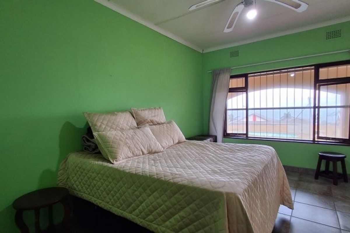 A bedroom featuring tiled flooring, a ceiling fan, and large windows with security bars, offering a view of the outdoor pool area.
