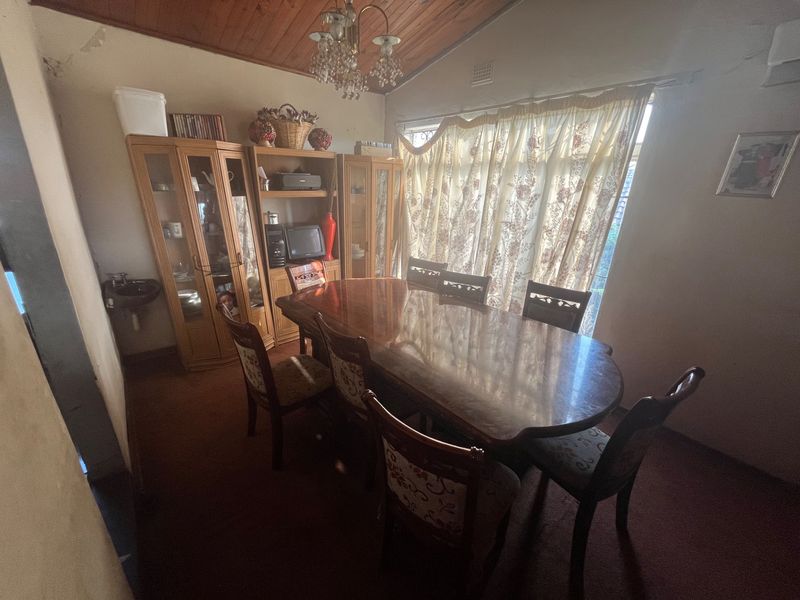 A dining room featuring a vaulted timber ceiling, carpeted flooring, and a small wall-mounted basin, offering a traditional layout with natural light.