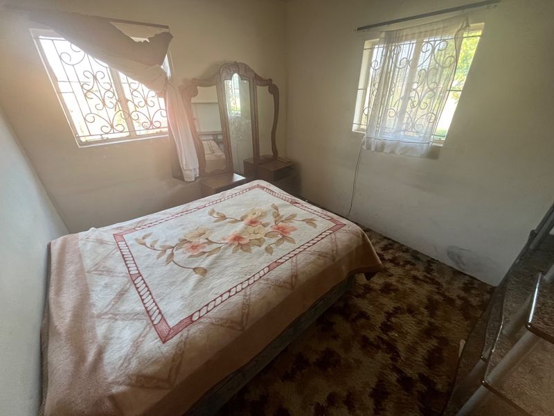 A bedroom featuring dual windows with security bars, carpeted flooring, and neutral wall finishes, offering a functional space ready for modernization.