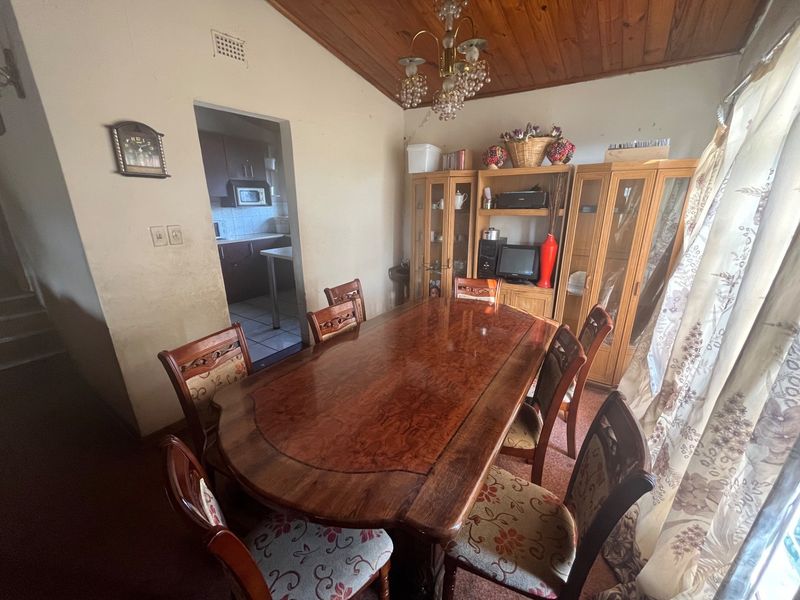 A dining room featuring a timber-paneled ceiling and chandelier, with an adjacent view into the kitchen area.