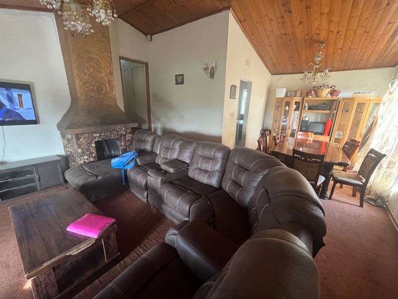 Open plan living and dining area featuring a built-in fireplace, vaulted wood-paneled ceilings, and carpeted flooring.