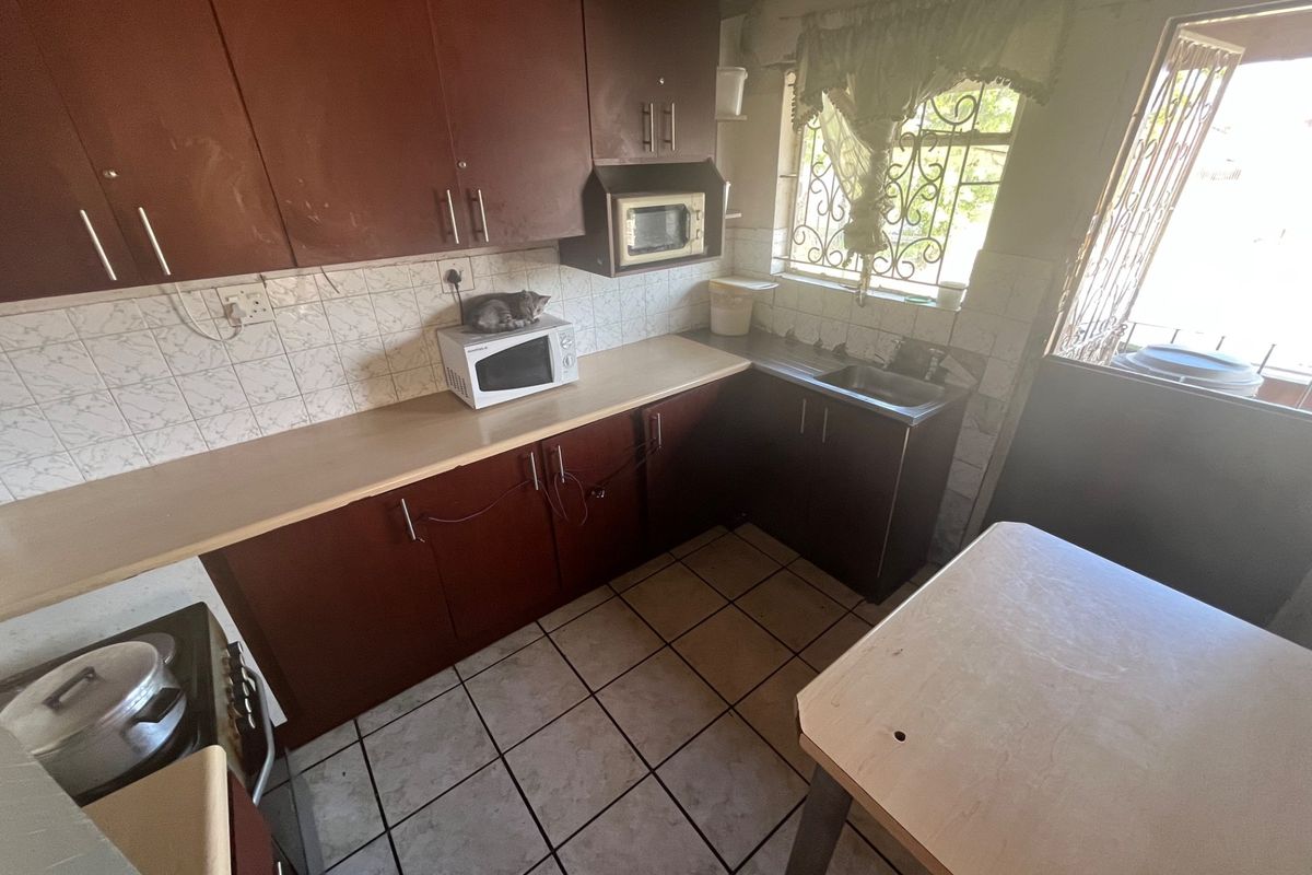 A functional kitchen featuring dark wood cabinetry, laminate countertops, tiled flooring, and a built-in microwave space with direct access to the exterior.
