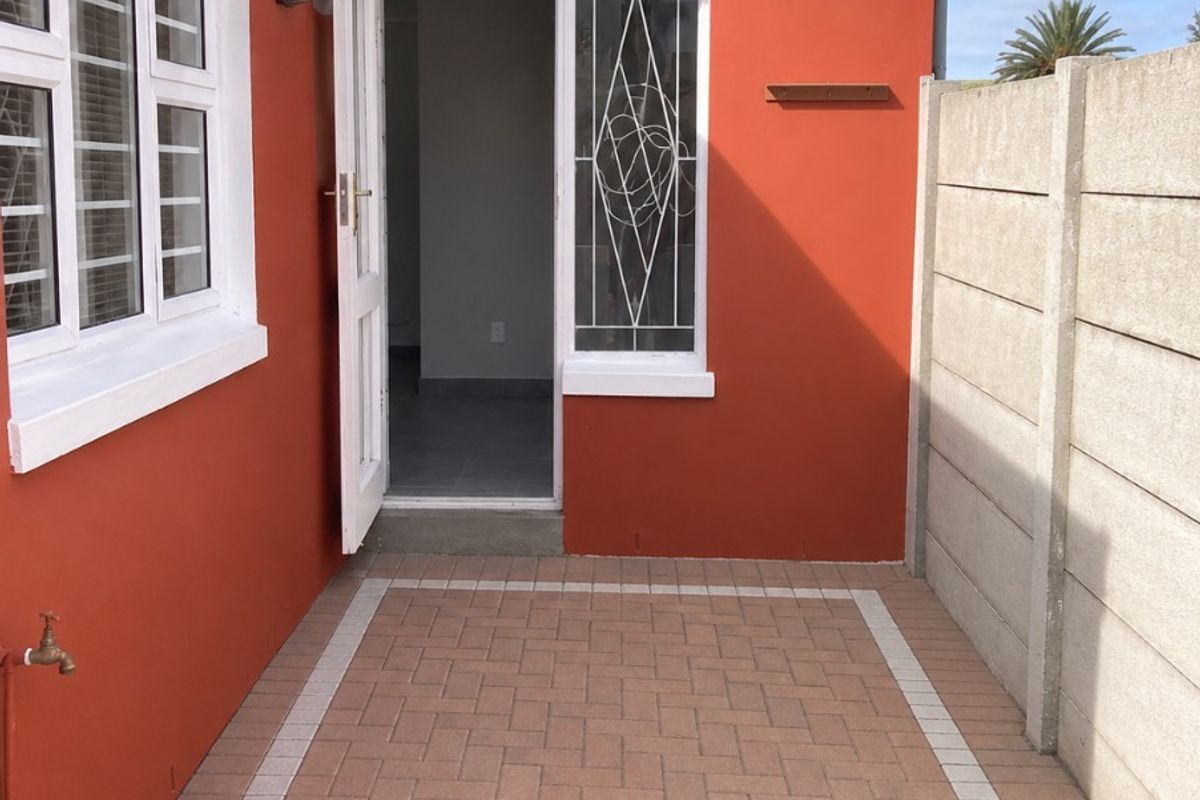 A neat rear exterior area featuring a paved patio, secure access door with security gate, and a precast concrete boundary wall.
