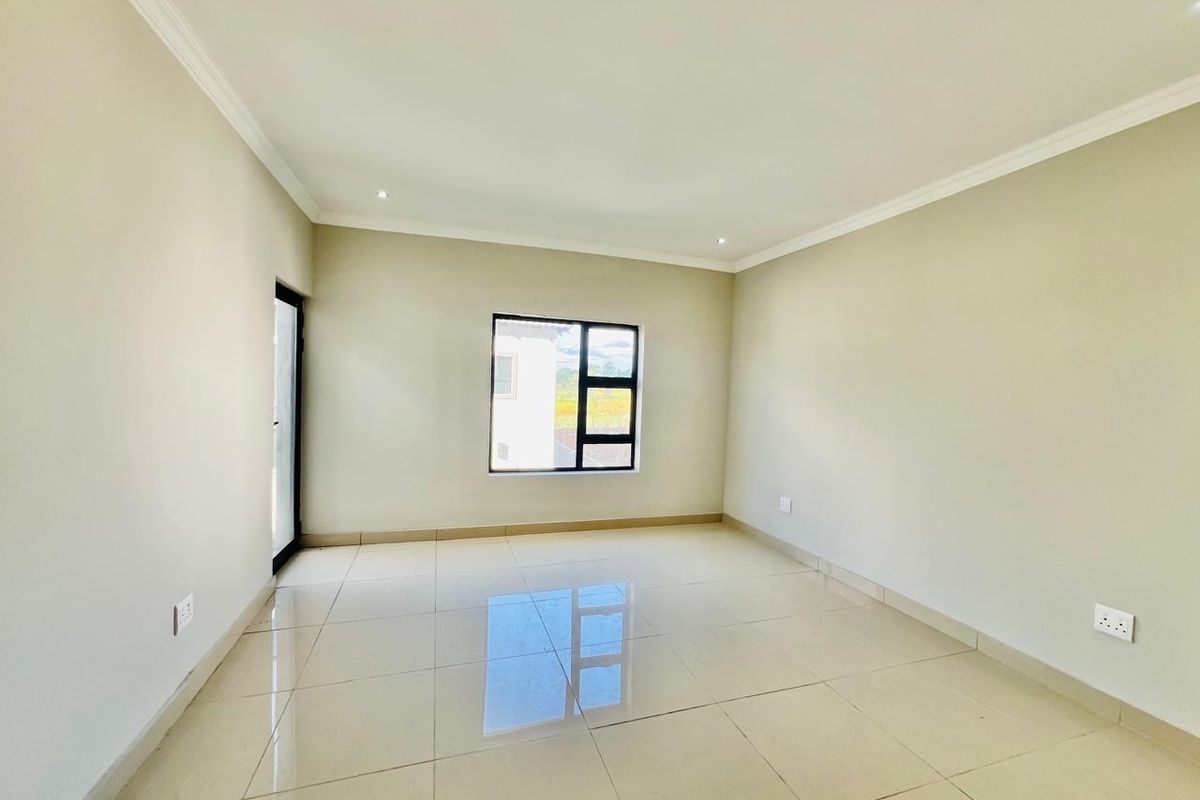 A bright, empty living room featuring neutral tiled flooring, recessed ceiling lighting, and a modern black-framed window.