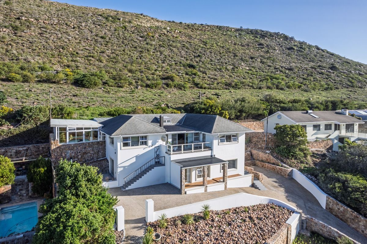 Aerial view of a multi-level residential property featuring a tiled roof, stone retaining walls, a swimming pool, and a paved driveway.