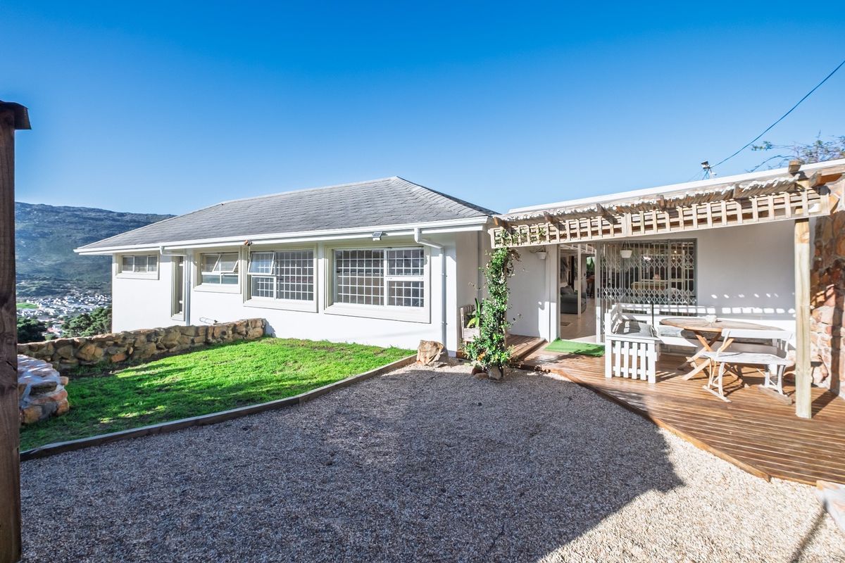 Rear exterior view featuring a wooden deck, pergola, gravel garden area, and stone retaining wall with mountain views.