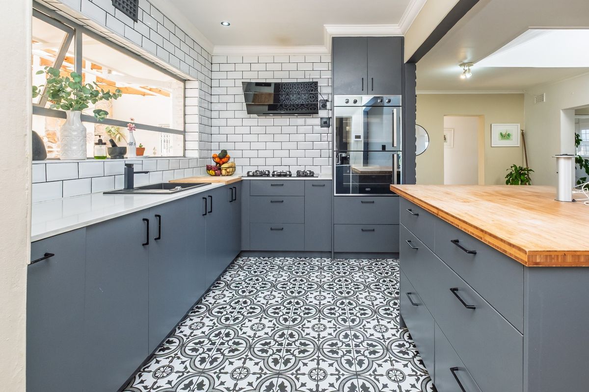 Modern kitchen featuring dark grey cabinetry, subway tile backsplash, patterned floor tiles, wooden countertops, and built-in oven with gas hob.
