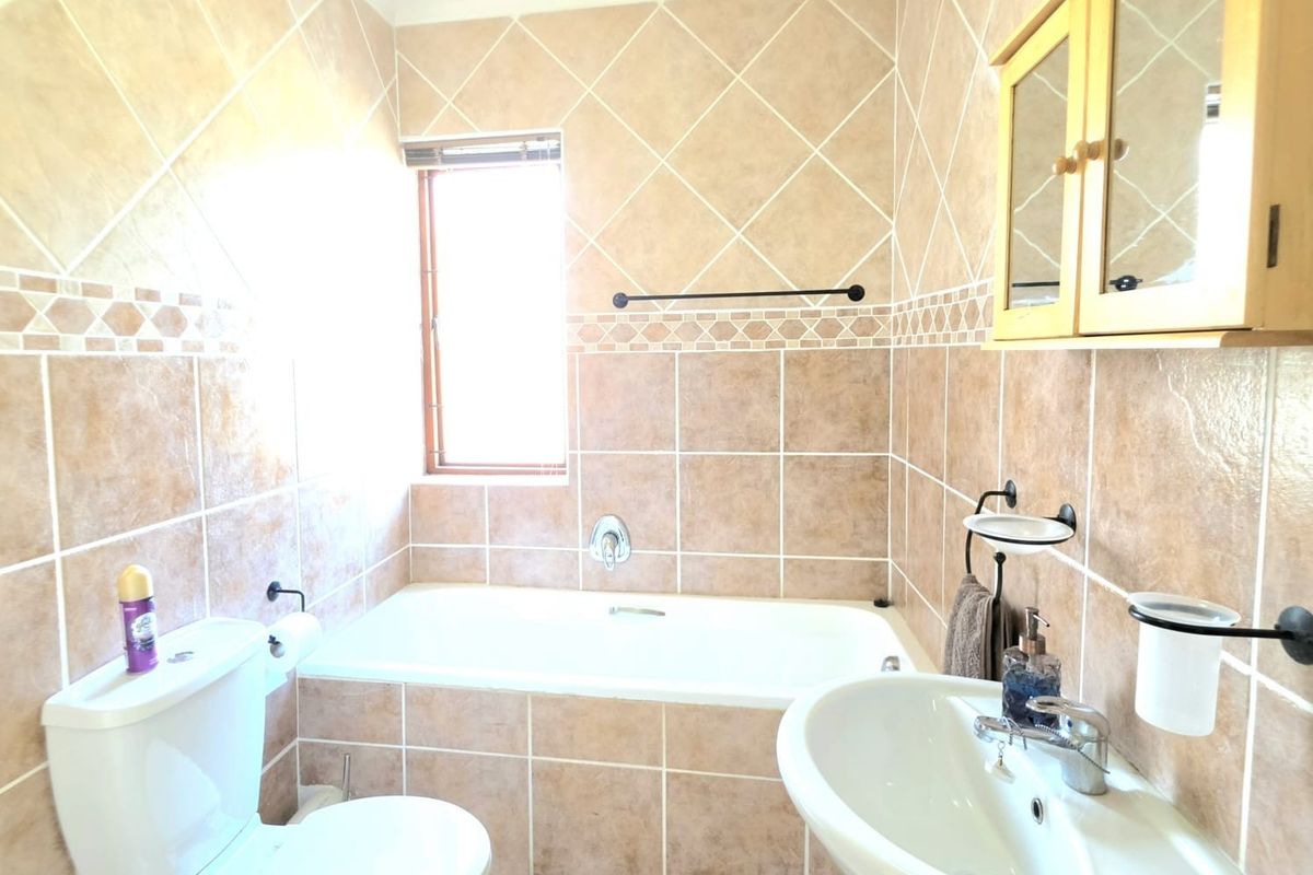 A functional bathroom featuring a built-in bathtub, pedestal sink, and wall-mounted medicine cabinet, finished with neutral ceramic wall tiling.