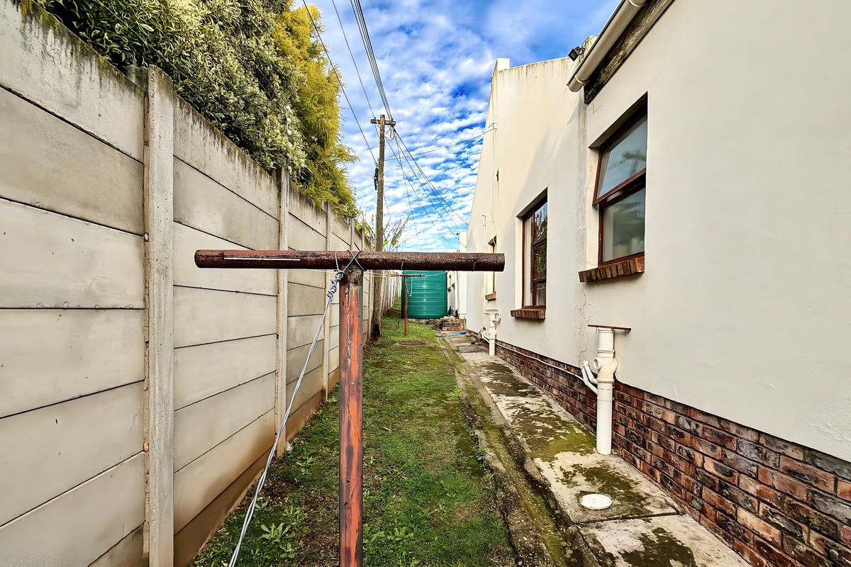 A narrow rear exterior side passage featuring a precast boundary wall, a metal washing line, and a water storage tank.