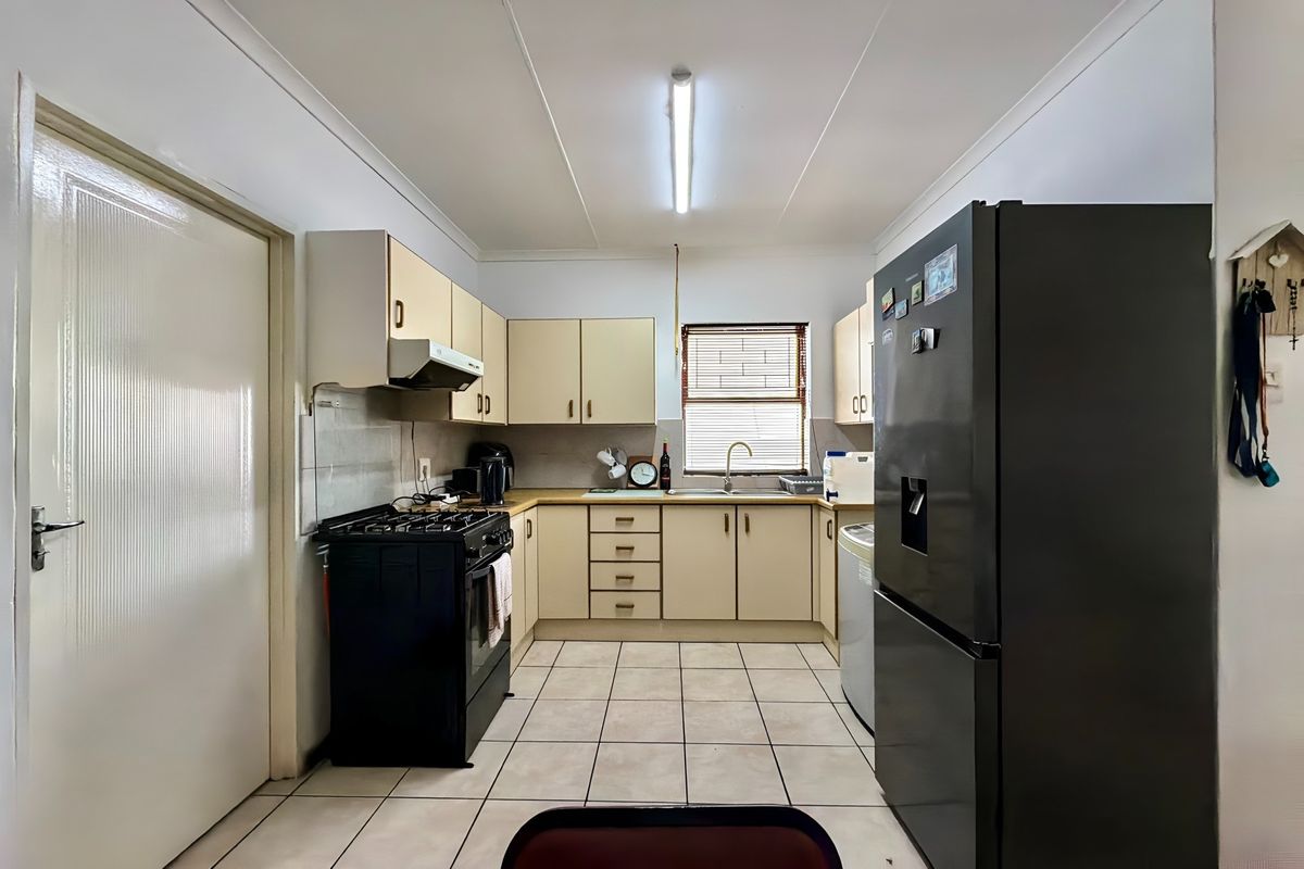A functional kitchen featuring light-toned cabinetry, tiled flooring, and a practical layout with a freestanding stove and integrated sink area.