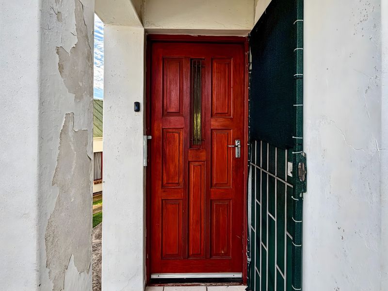 Front entrance featuring a timber door and security gate, currently showing significant exterior paint deterioration and wall finish damage requiring maintenance.