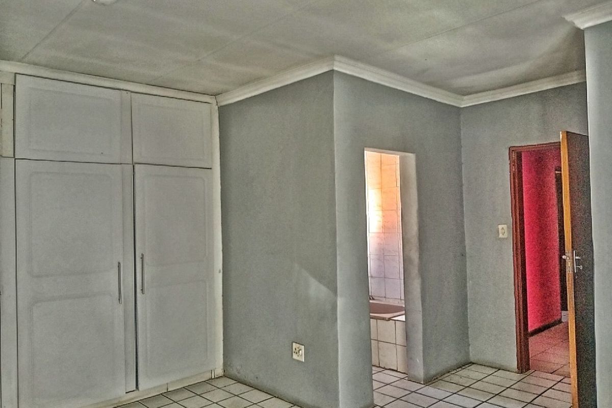 An empty bedroom featuring built-in cupboards, tiled flooring, and direct access to an en-suite bathroom area.
