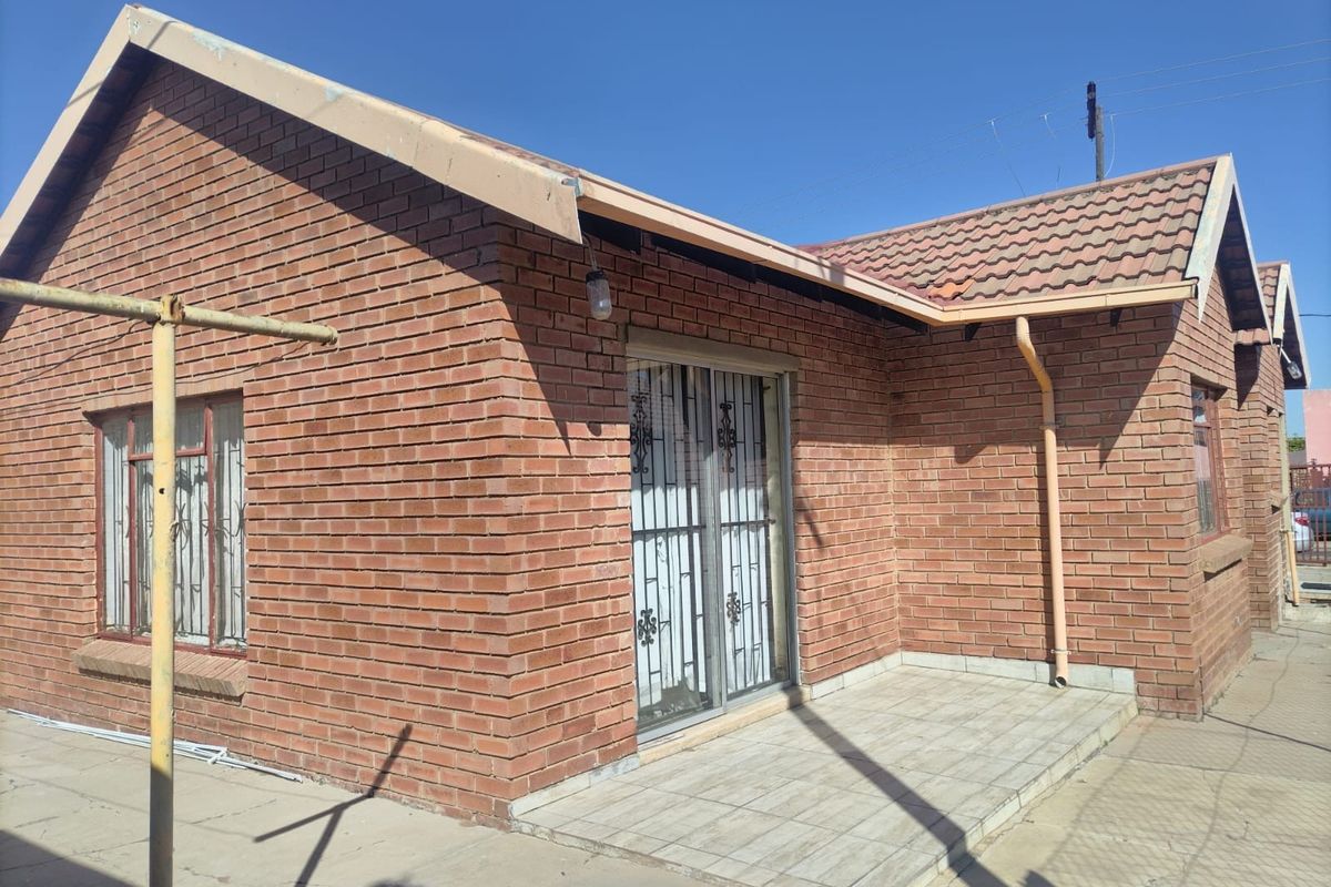 Rear view of a face brick house featuring a tiled patio, sliding glass door with security gate, and a concrete apron.