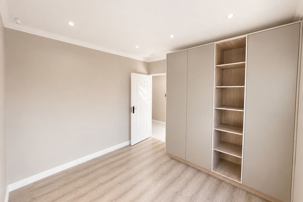 A bright, modern bedroom featuring neutral walls, light wood-look laminate flooring, and a large, contemporary built-in wardrobe with open shelving.