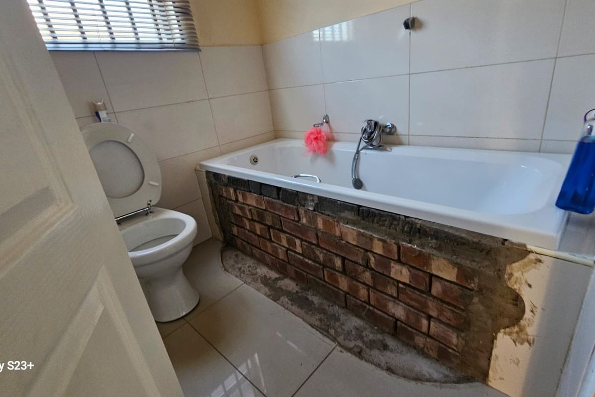 A bathroom featuring a standard toilet and a bathtub with an unfinished, exposed brick apron requiring tiling or cladding.