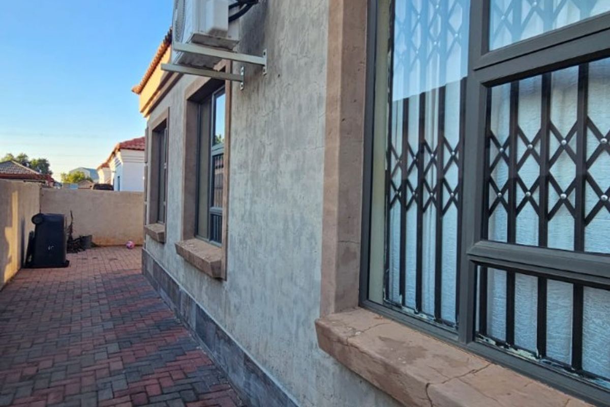 Side exterior view of the house featuring paved walkway, security bars on windows, and a wall-mounted air conditioning unit.