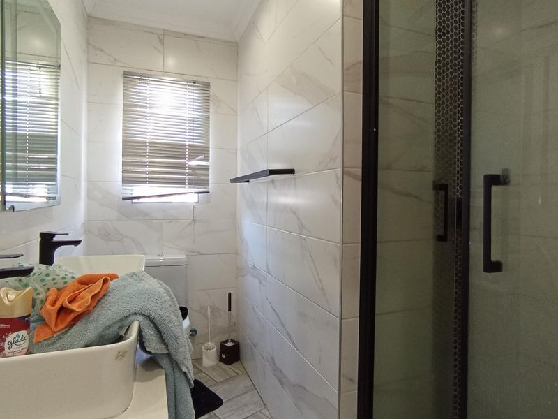 Modern bathroom featuring marble-look wall tiles, a walk-in shower with a black frame, a vessel sink with a black mixer, and a toilet.