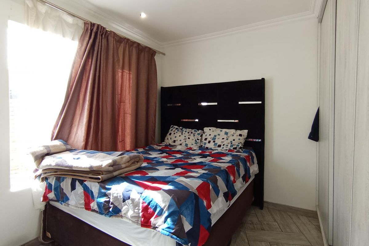 A well-lit bedroom featuring tiled flooring, built-in cupboards, and decorative ceiling cornicing.