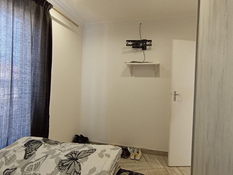 A bedroom featuring tiled flooring, a built-in wardrobe, and a wall-mounted TV bracket with a small shelf.
