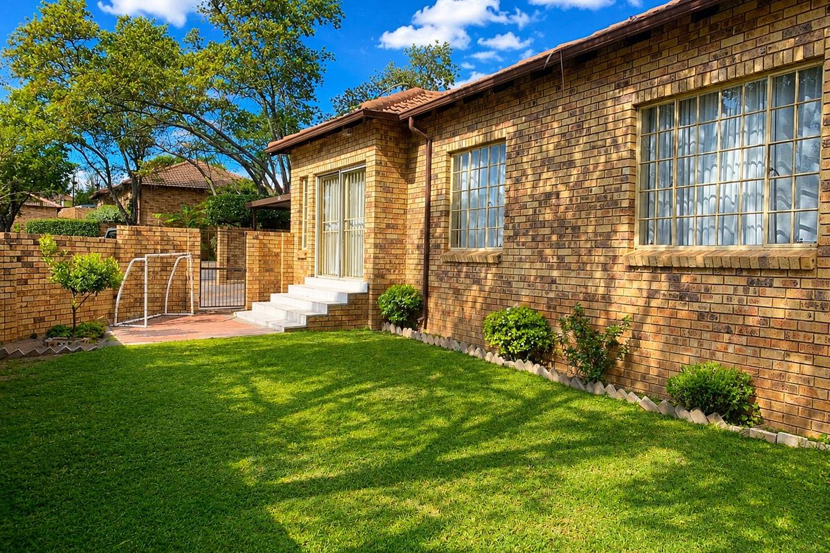 A well-maintained rear garden featuring a brick facade, tiled patio steps, and secure perimeter walling with established lawn.