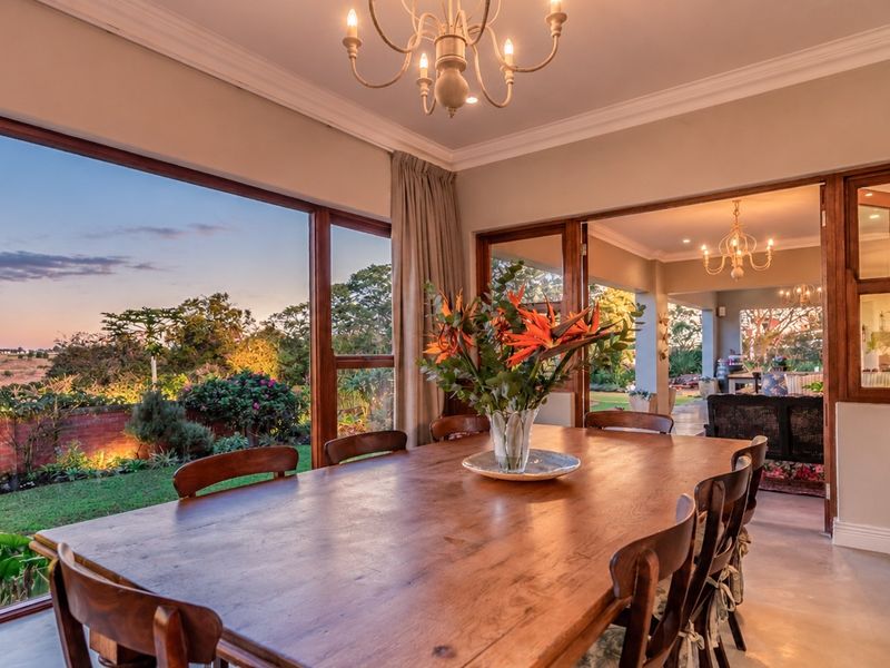 Elegant dining room featuring polished concrete floors, crown molding, and expansive timber-framed windows offering seamless views of the landscaped garden and patio area.