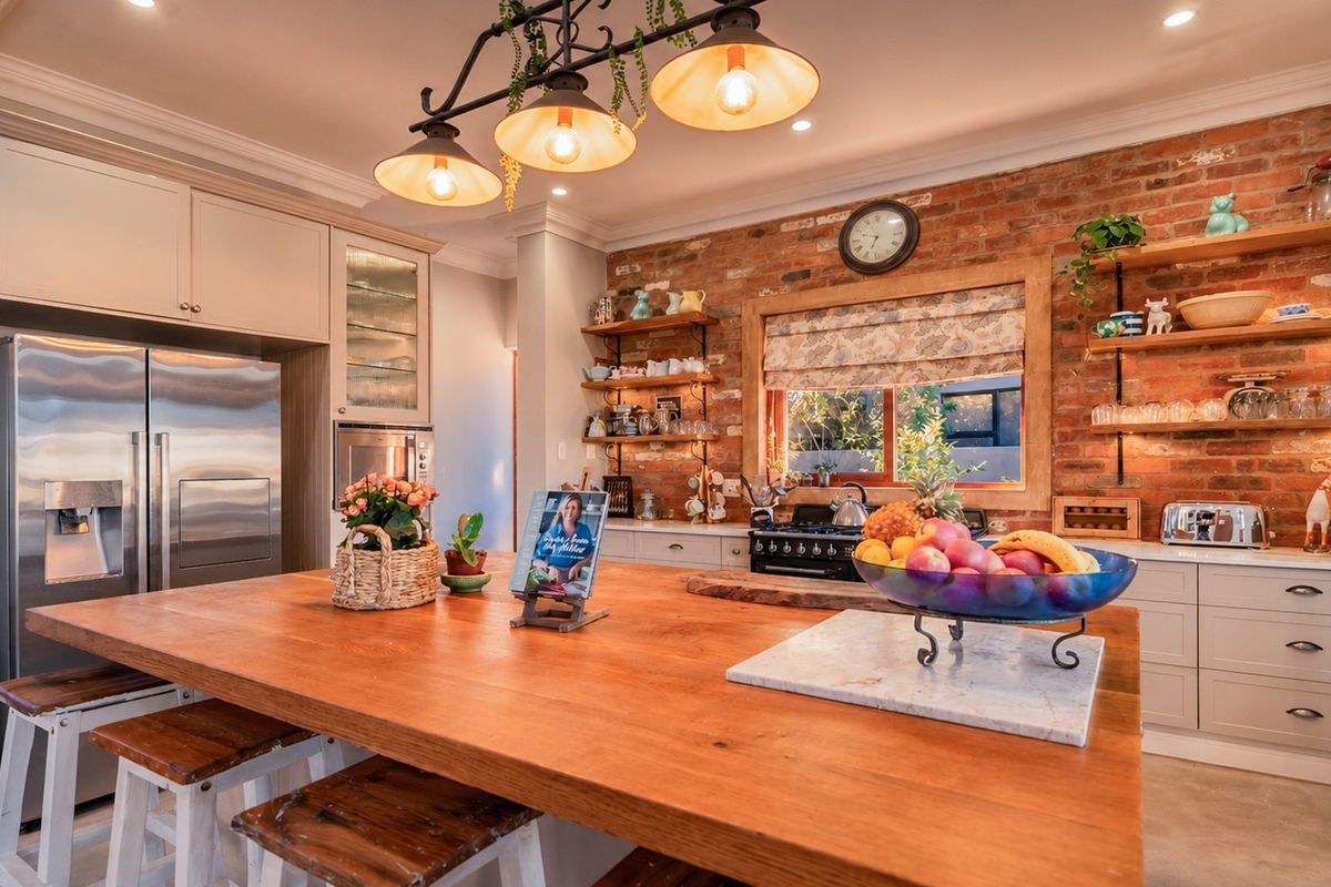 A charming kitchen featuring an exposed brick wall, a large wooden island, custom cabinetry, and warm pendant lighting.
