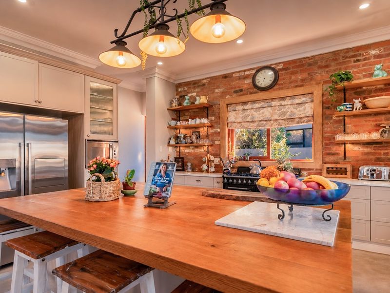A charming kitchen featuring an exposed brick wall, a large wooden island, custom cabinetry, and warm pendant lighting.