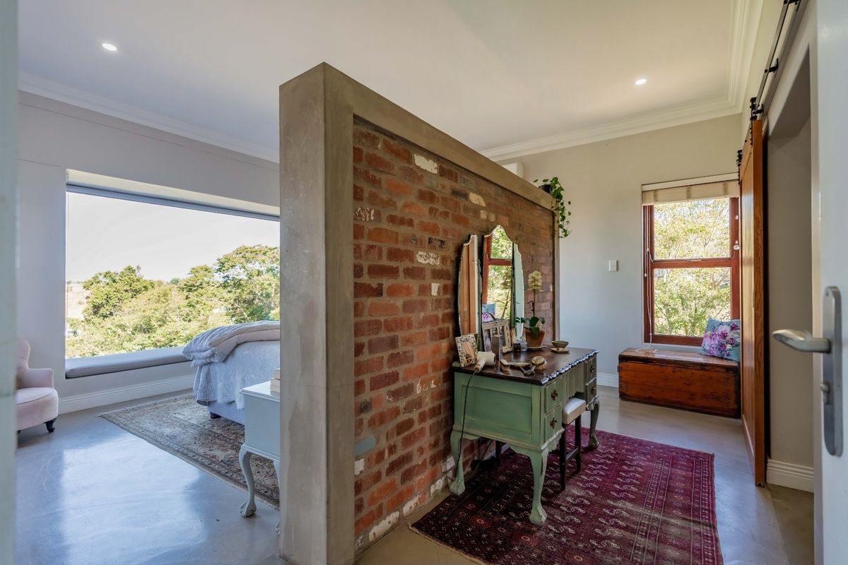 Spacious bedroom featuring a unique exposed brick partition wall, polished concrete floors, and a built-in window seat with scenic views.