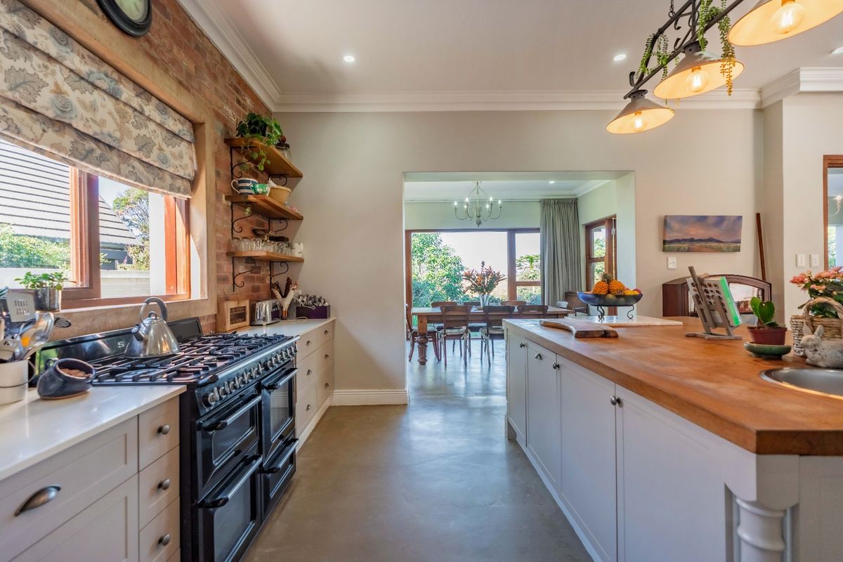 A well-appointed kitchen featuring a large island with a butcher block countertop, gas range cooker, and exposed brick wall, flowing into the dining area.