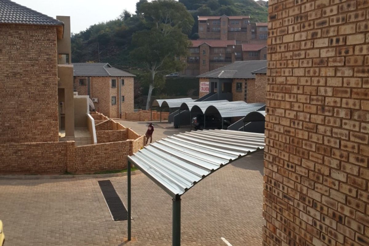 View of the apartment complex exterior featuring paved driveway, covered parking bays, and face-brick building facades.