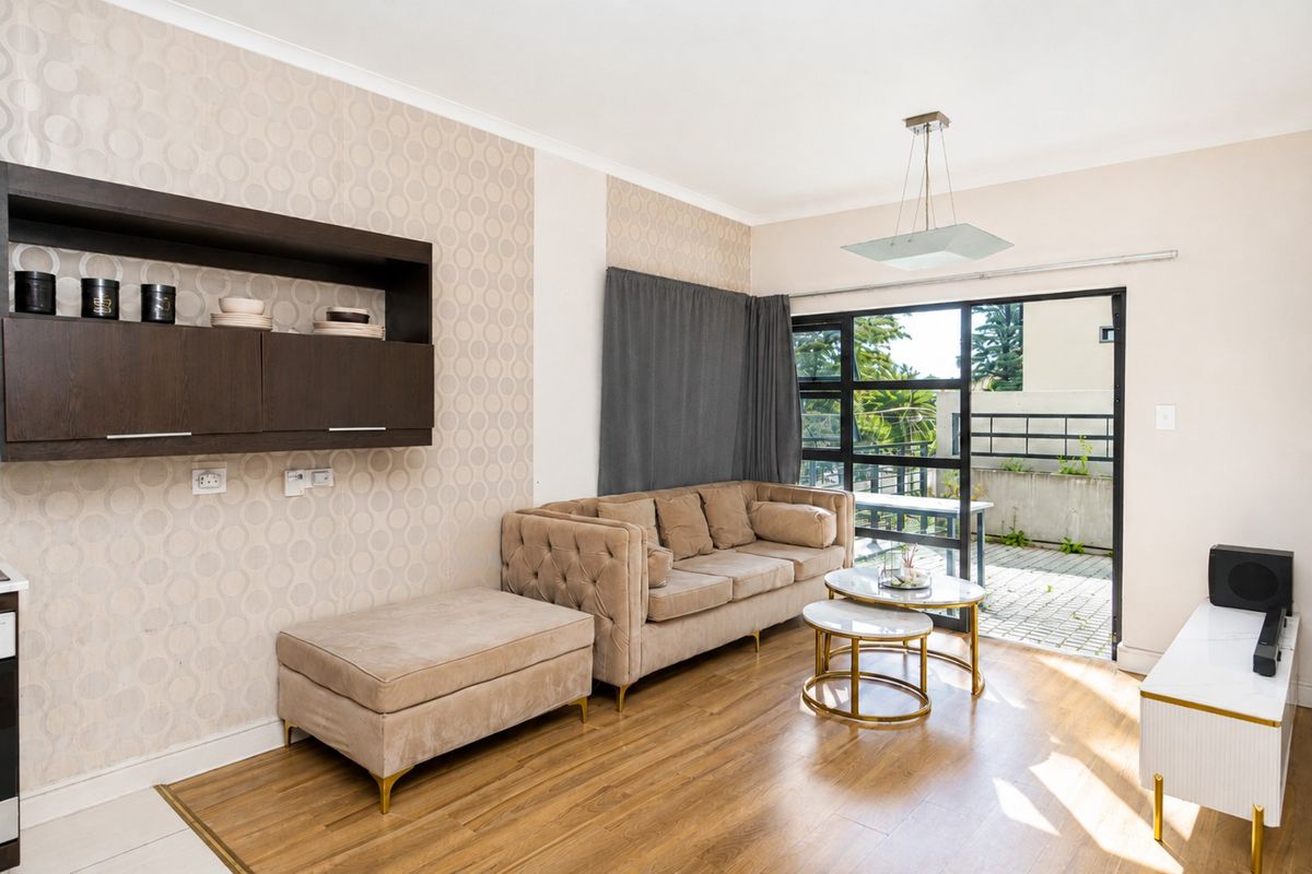 A bright living room featuring wood-look flooring, patterned wallpaper, and large sliding glass doors that open onto a private patio area.