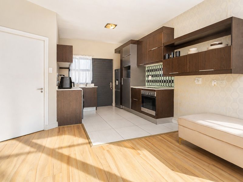 Open-plan kitchen featuring dark wood cabinetry, built-in oven and hob, tiled flooring, and a seamless transition to the living area.