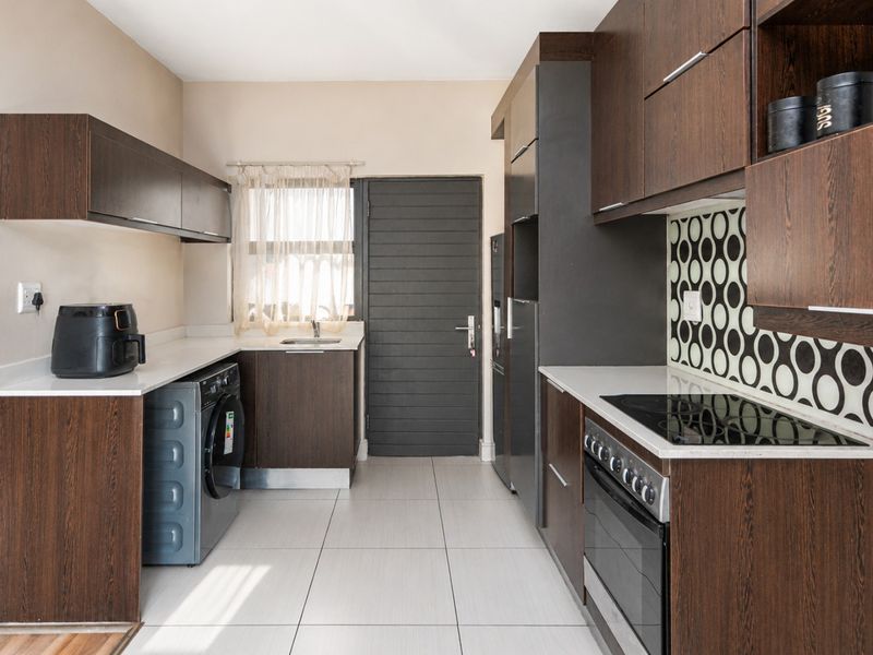 Modern kitchen featuring dark wood cabinetry, stone countertops, a built-in electric oven and hob, and a dedicated laundry area with plumbing connections.