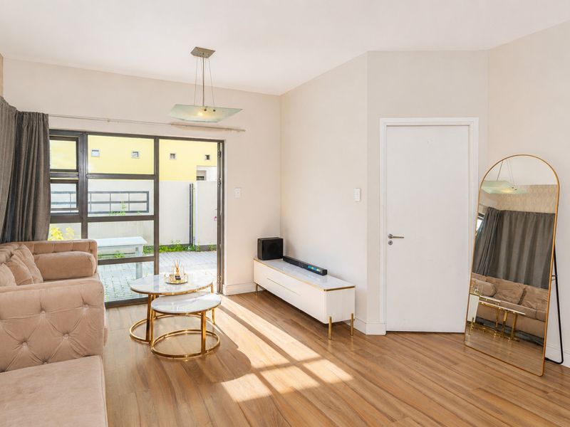 A bright living room featuring wood-look flooring, a modern pendant light, and large sliding glass doors providing direct access to an outdoor patio area.