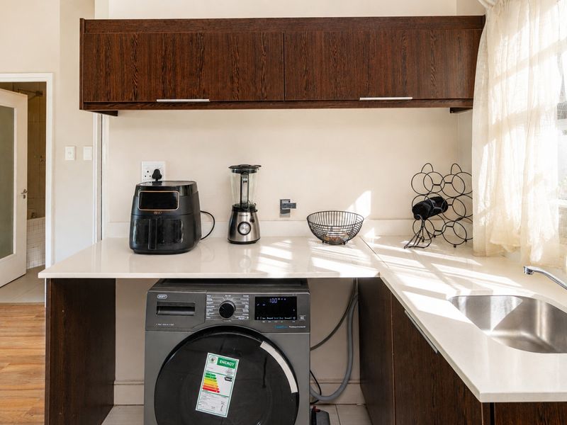 A functional laundry area featuring dark wood cabinetry, light stone countertops, a stainless steel sink, and space for a front-loading washing machine.