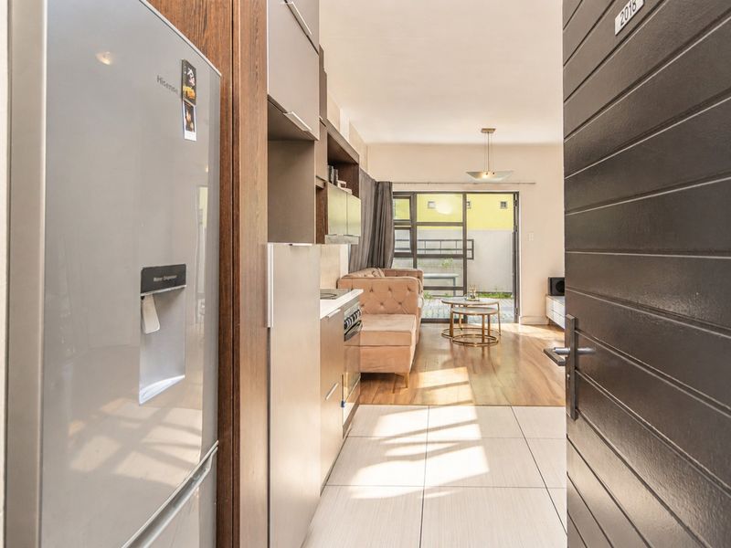 Open-plan apartment entrance leading into a modern kitchen area with tiled flooring, flowing into a living space with direct access to a patio.
