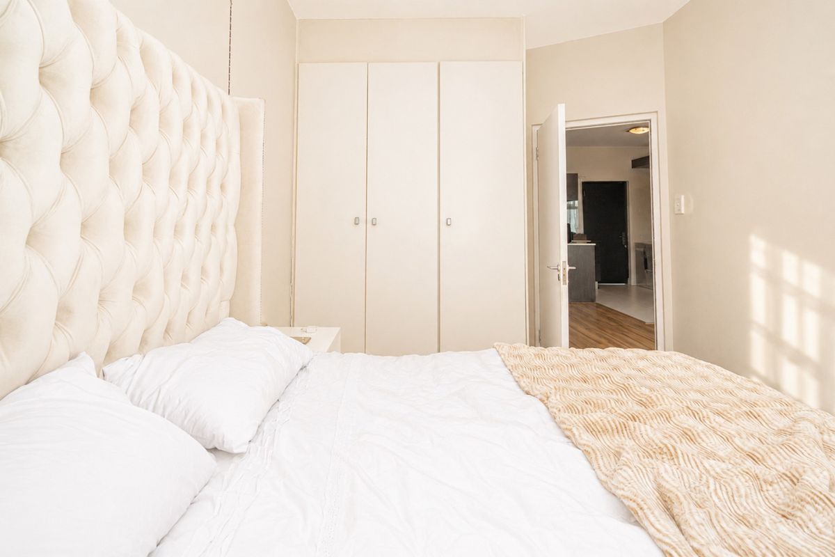 A well-maintained bedroom featuring built-in cupboards and neutral finishes, with a view through the doorway into the adjacent living area.